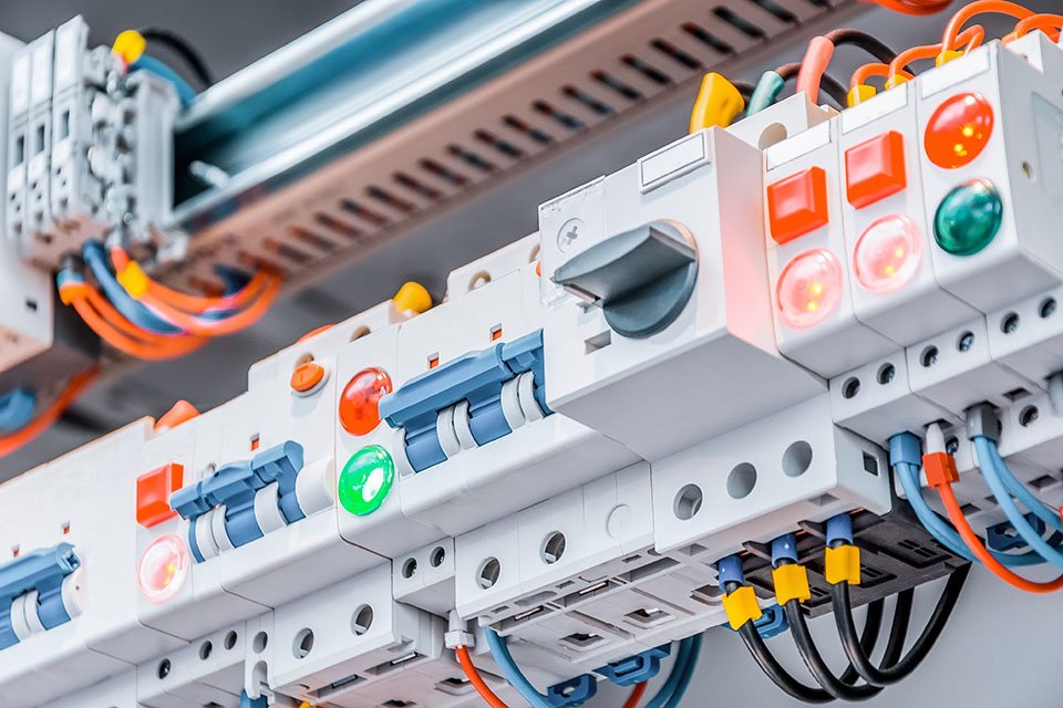 Industrial electrical control panel with circuit breakers, colored wiring, and illuminated safety indicators, representing preventive inspection and maintenance to ensure reliable and safe power systems.