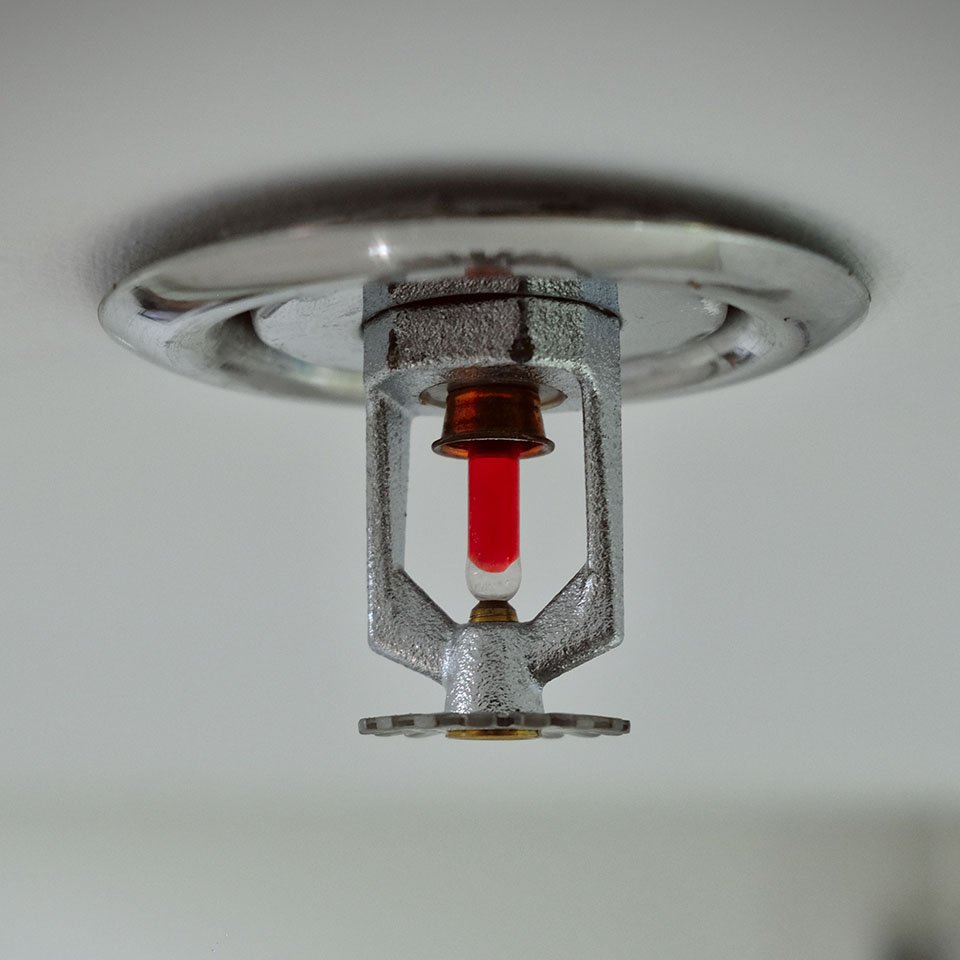Ceiling‑mounted fire sprinkler head with heat‑sensitive bulb and deflector plate, representing installation and maintenance of fire alarm and safety systems in industrial and commercial buildings.