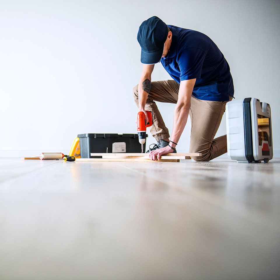 Technician using a power drill on wooden flooring with tools nearby, representing professional construction and renovation services for industrial and commercial facilities.